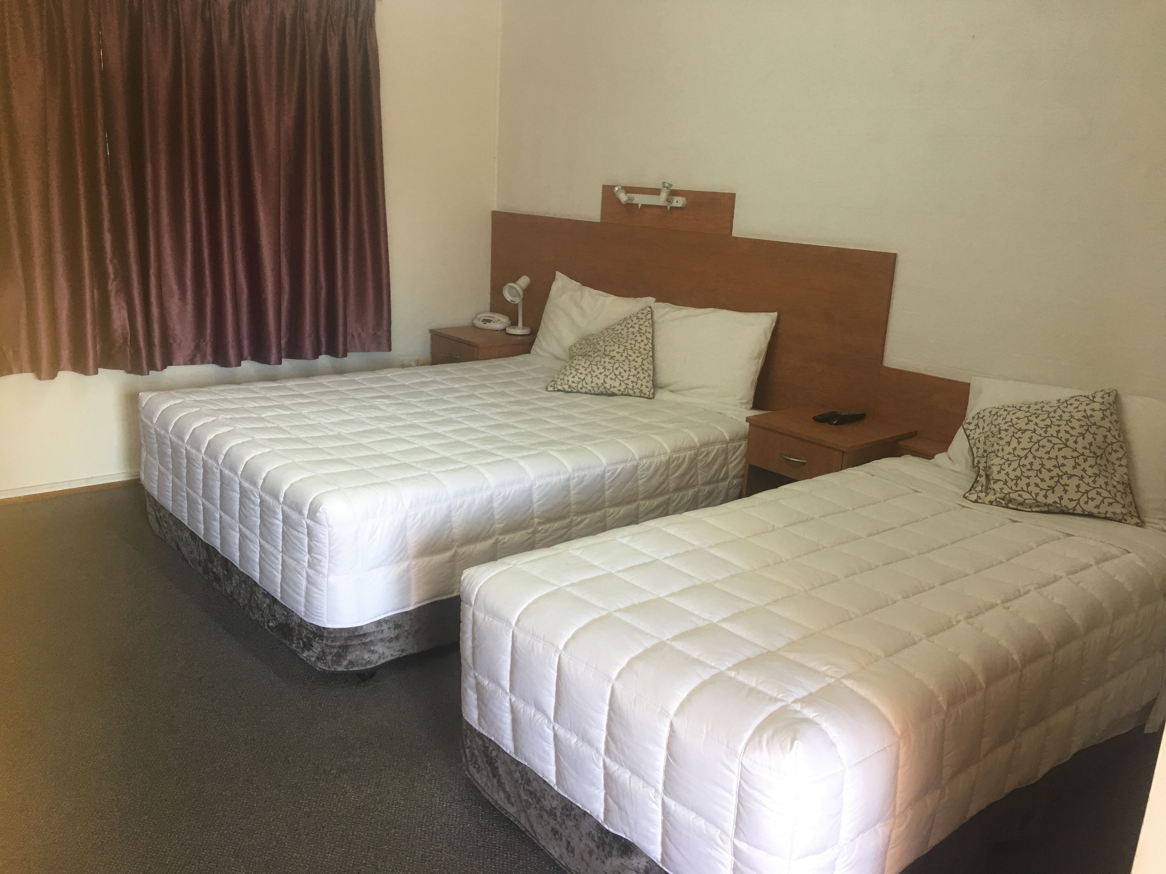 Una habitación de hotel con dos camas, una mesita de noche con lámpara y una ventana con cortinas.