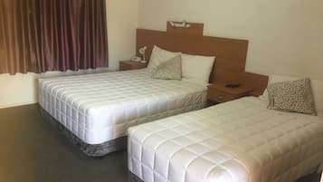 Una habitación de hotel con dos camas, una mesita de noche con lámpara y una ventana con cortinas.
