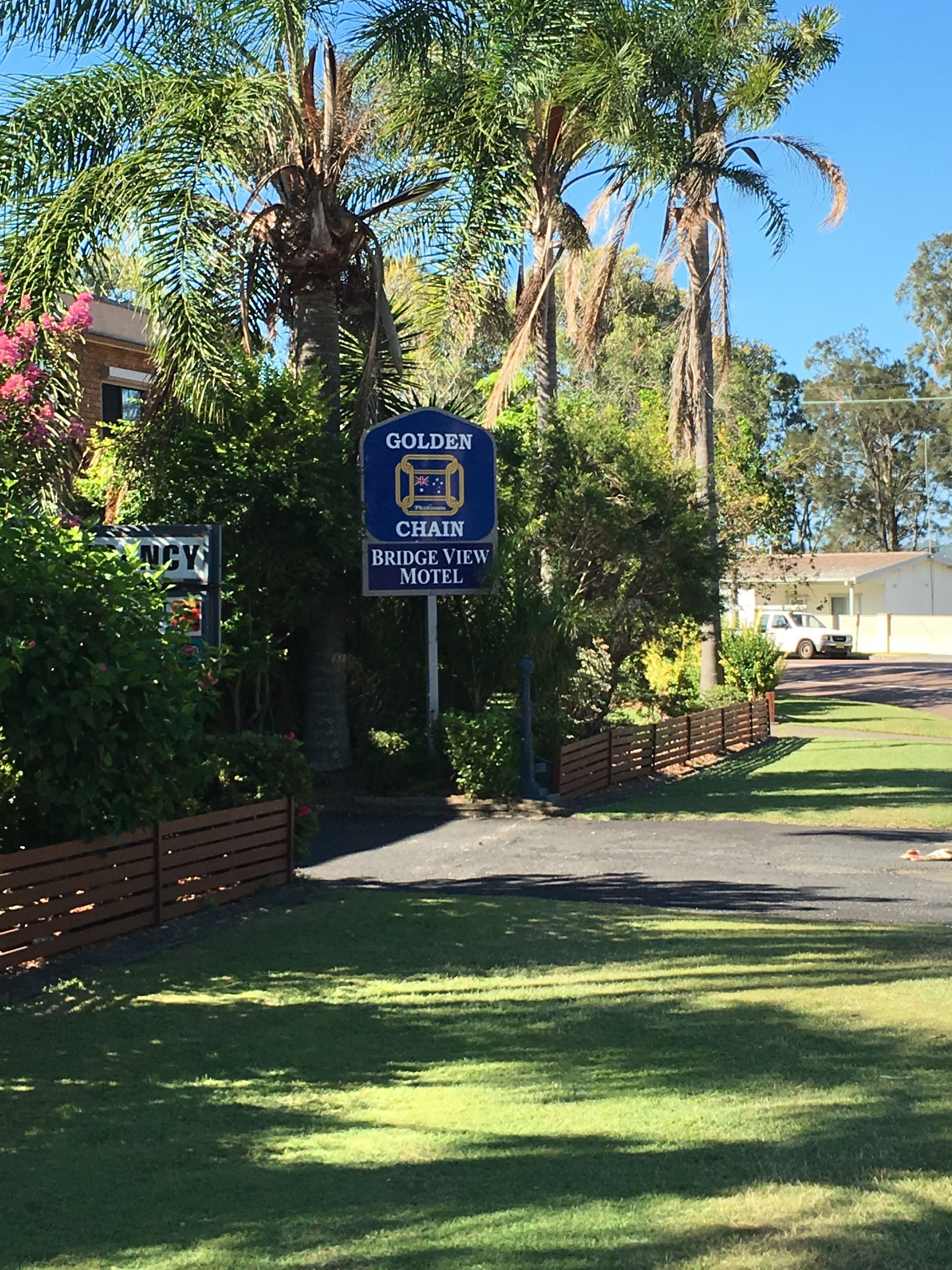 A sign for the Golden Chain Bridge View Motel, surrounded by lush greenery and palm trees.