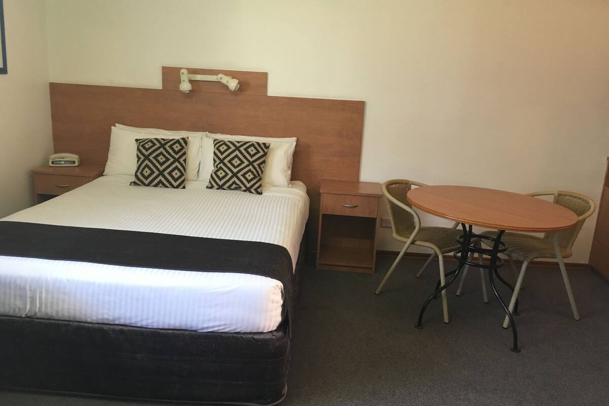A hotel room with a bed, bedside table, chair, and a small table with a chair.