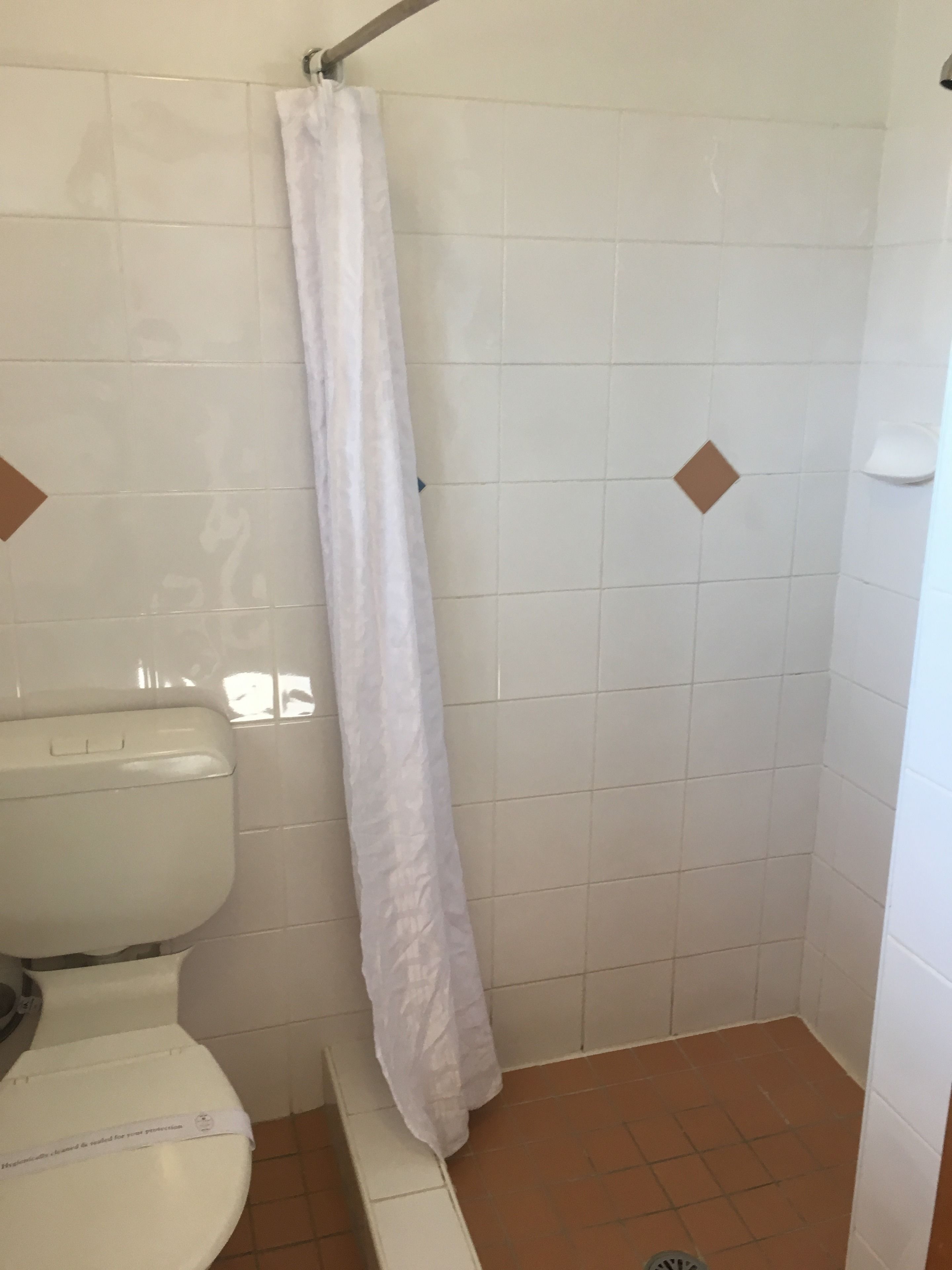 Un petit espace douche fermé, avec des toilettes blanches et un rideau de douche.
