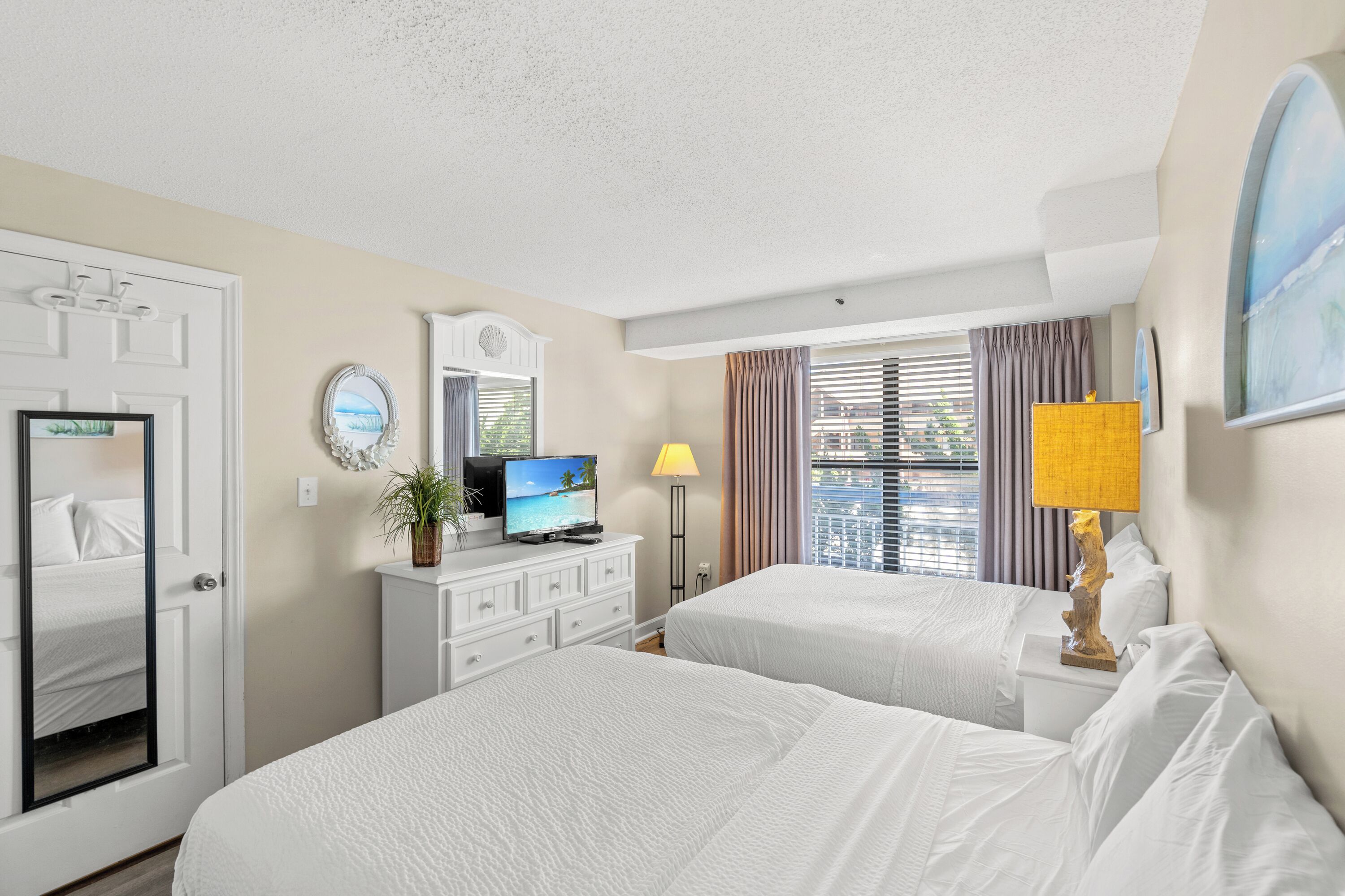 Een hotelkamer met twee bedden, een televisie, een bureau en een raam met gordijnen.