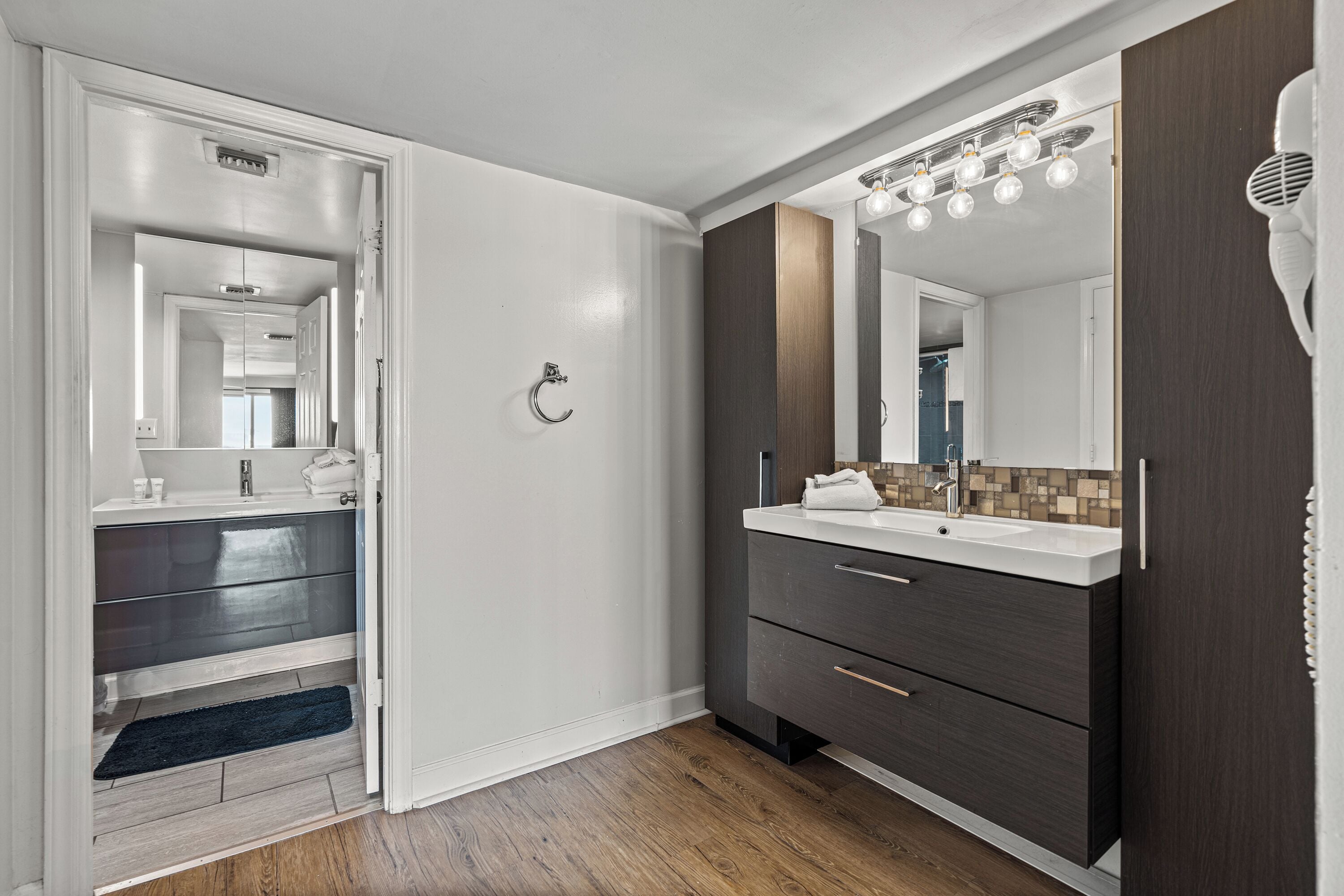 A modern bathroom with a double sink vanity, a large mirror, and a hairdryer mounted on the wall.