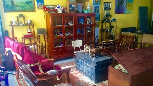 A cozy living room with a red sofa, wooden chairs, a coffee table, and a bookshelf filled with various items. - Casa Ceasars  Historic Quito (Quito)