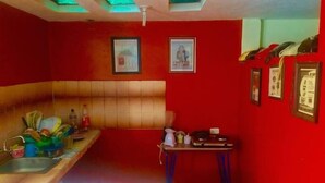 A kitchen with red walls, a tiled backsplash, and a sink. There are framed pictures on the wall and a small table with a kettle. - Casa Ceasars  Historic Quito (Quito)