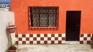 A building with a red exterior, a window with a metal grille, and a black door. - Casa Ceasars  Historic Quito (Quito)