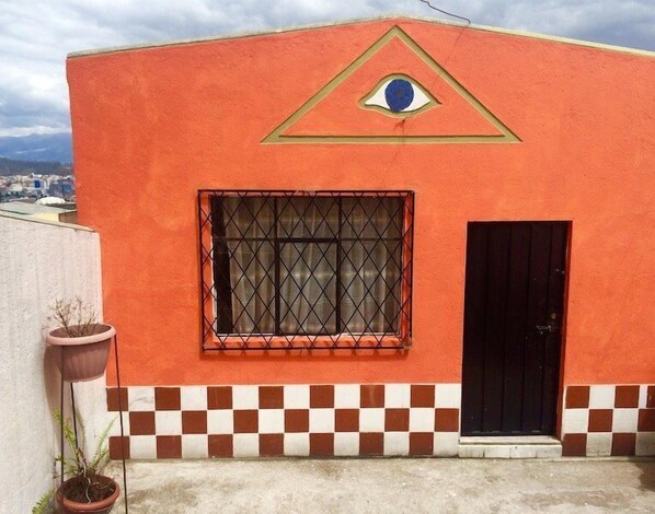 A building with a red exterior, a window with a metal grille, and a black door. - Casa Ceasars  Historic Quito (Quito)