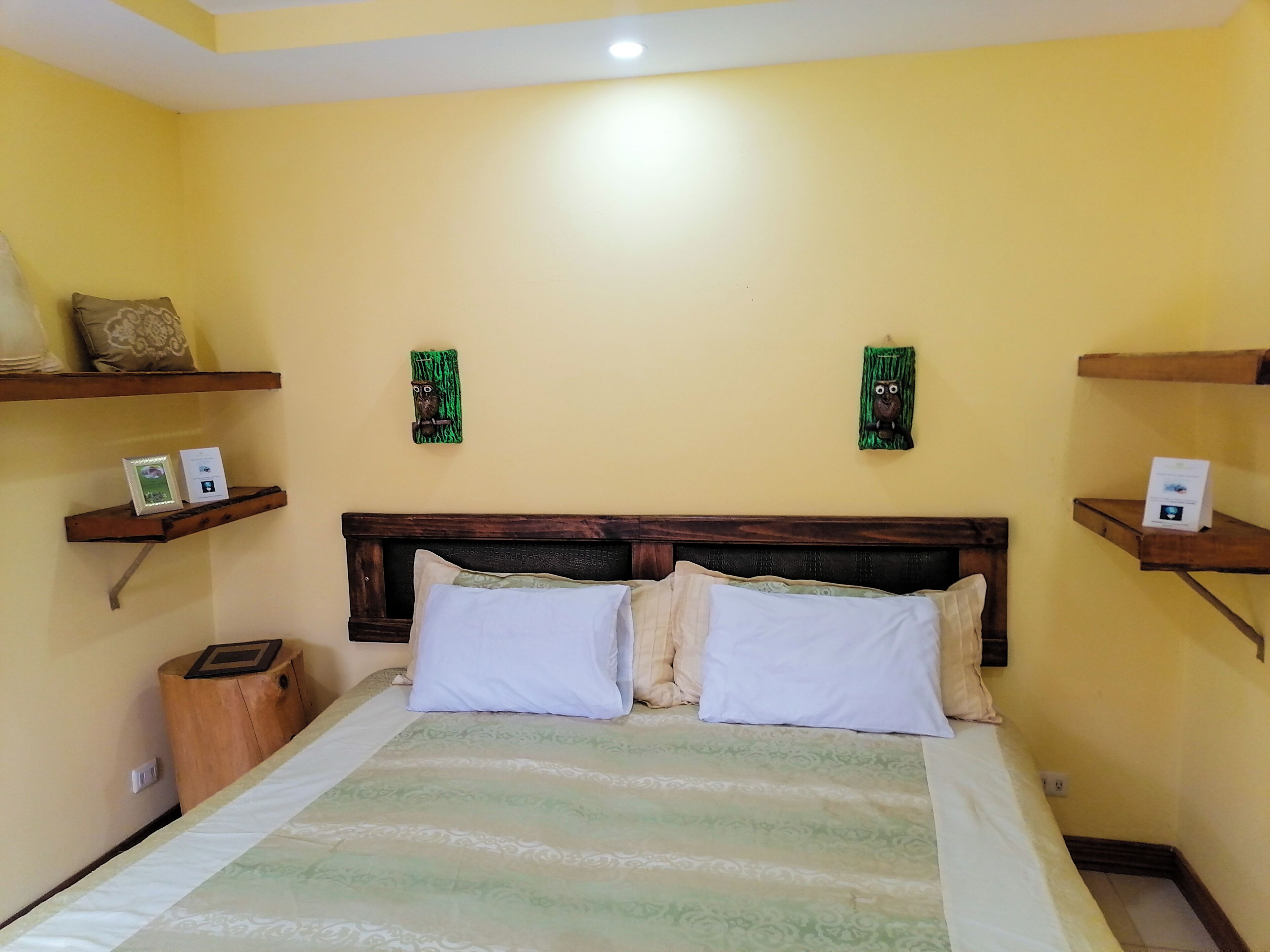 Una stanza con un letto, una testiera in legno, due cuscini, un comodino e due mensole a parete con oggetti decorativi.