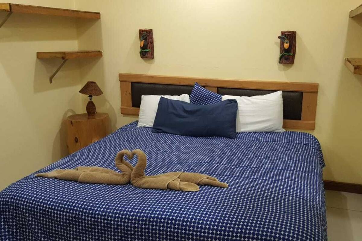 A neatly made bed with a blue patterned bedspread, two pillows, and a decorative swan towel arrangement.