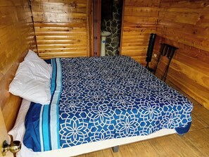 A wooden cabin room with a bed, a white pillow, and a patterned bedspread.