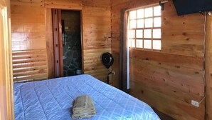 A wooden cabin room with a bed, a stone wall, a window, and a television. - Paraíso Orocay Lodge (Paraiso)