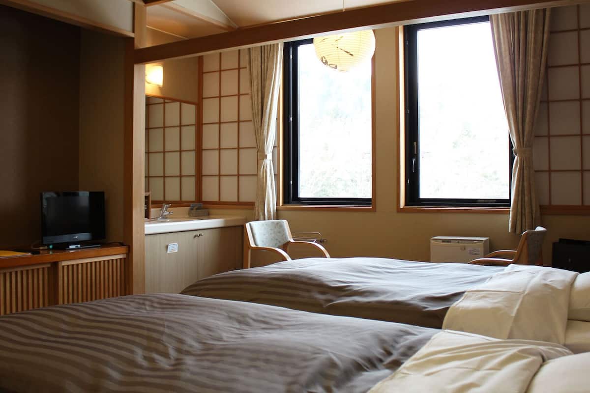 A hotel room with a bed, a desk with a TV, a chair, and a window with curtains.