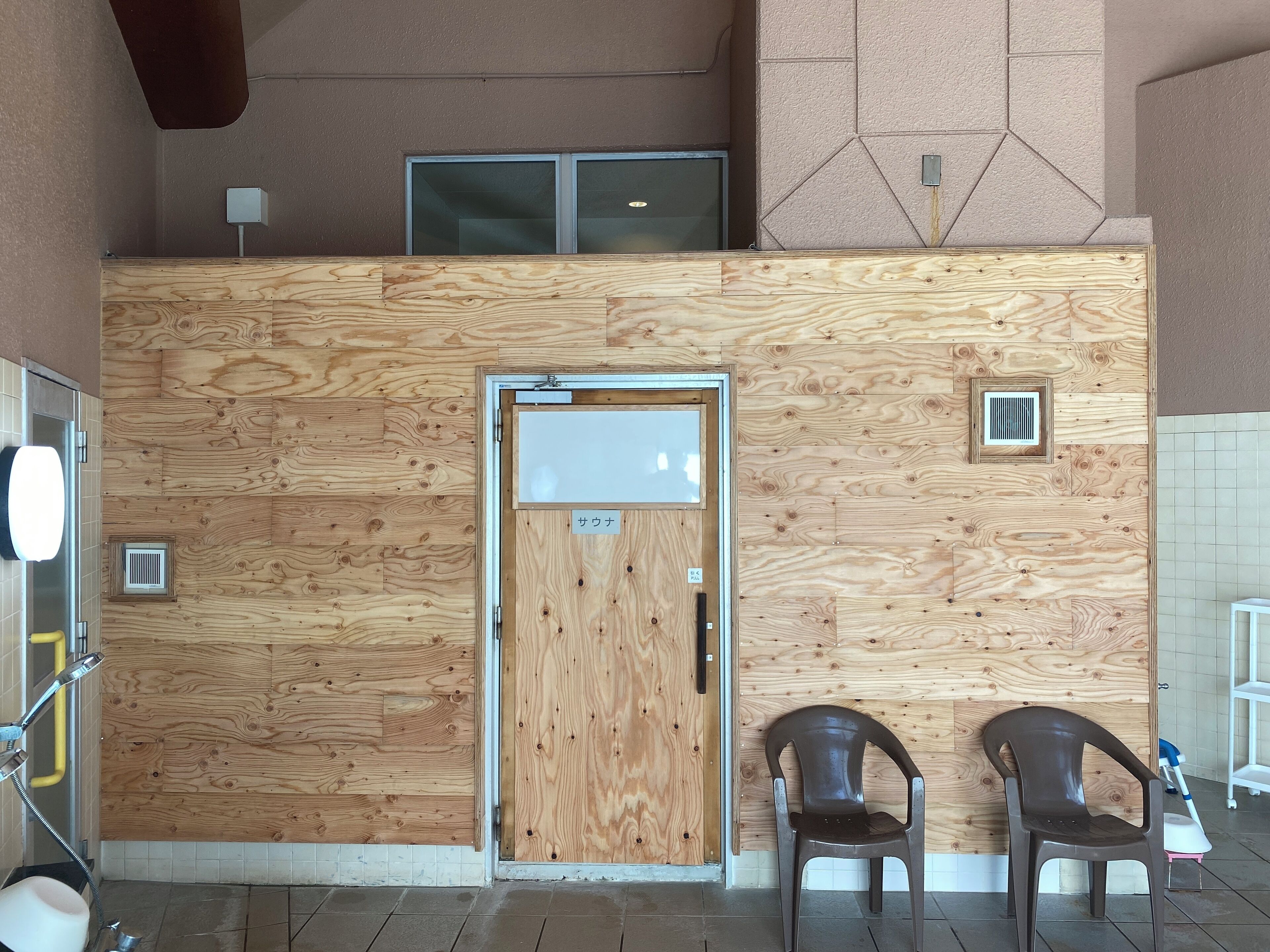 A room with a wooden wall panel, a door with a window, two plastic chairs, and a small table with a blue object.