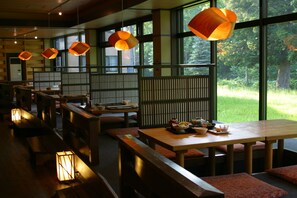 A restaurant with wooden furniture, large windows, and hanging lamps.