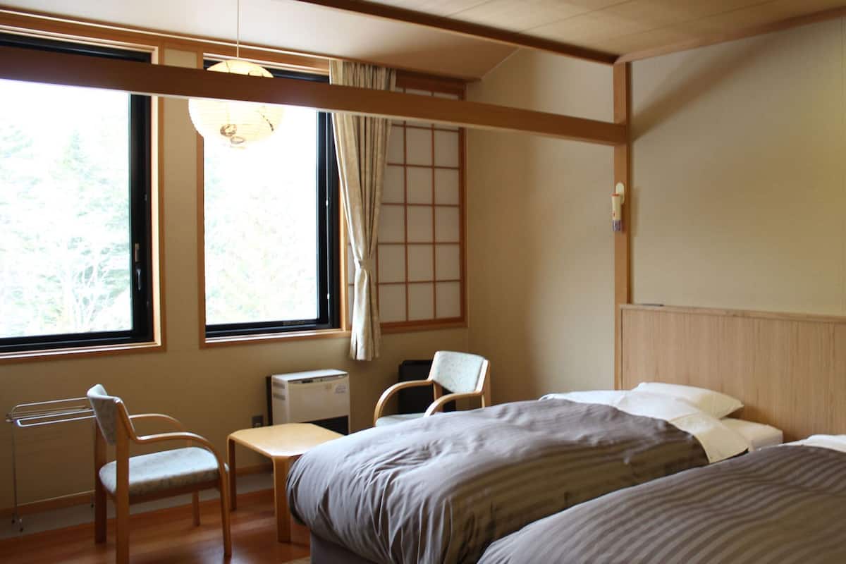A room with two beds, a chair, a table, a window with curtains, and a radiator.