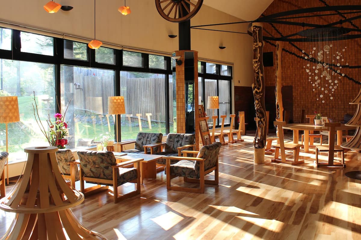 A spacious room with large windows, wooden furniture, and a unique wooden sculpture.