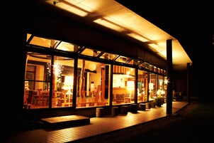 A modern building with large glass windows, a wooden deck, and outdoor seating.
