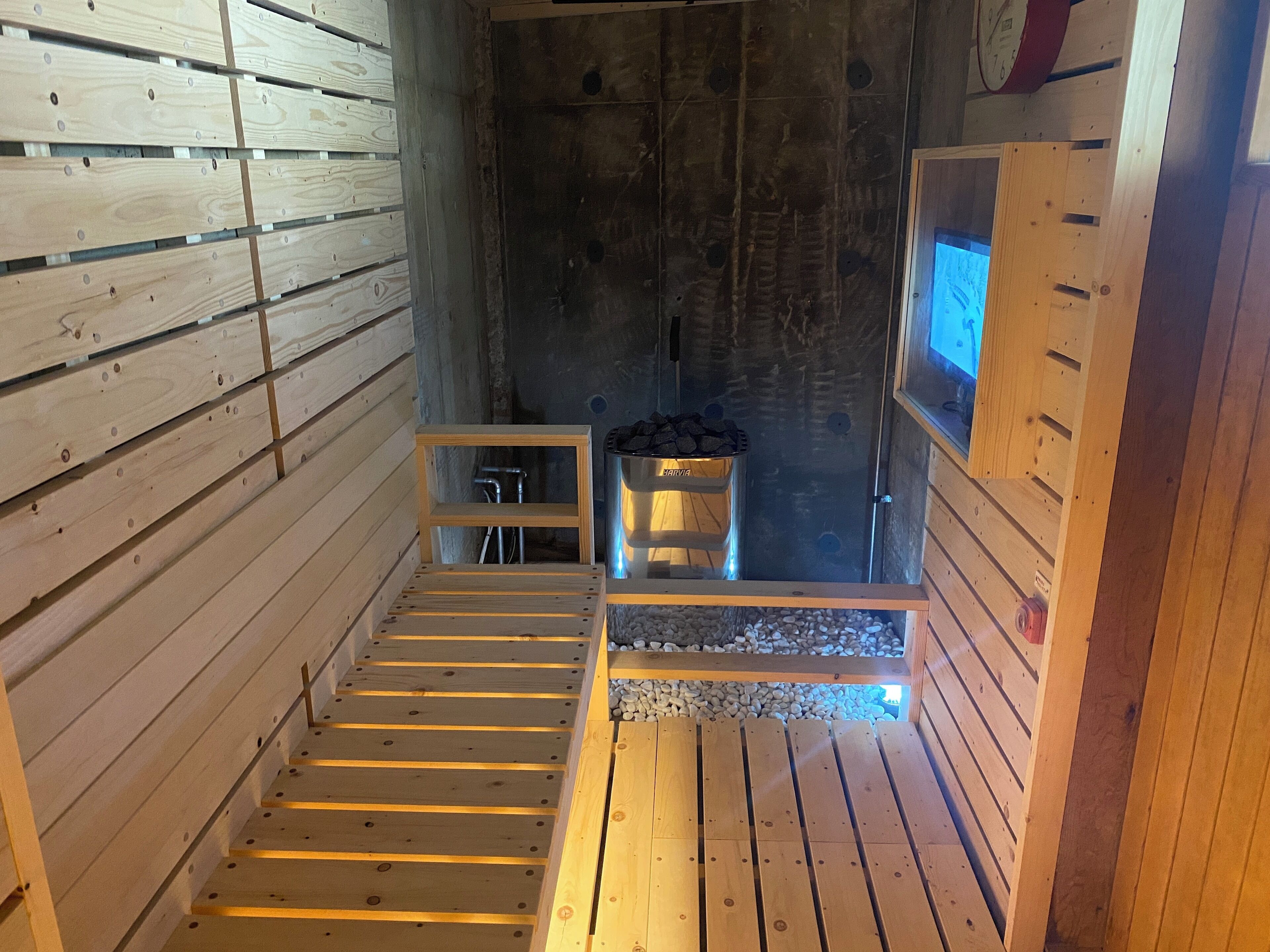 A sauna room with wooden benches, a metal container for wood, and a small table.