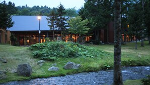 Un edificio moderno con fachada de vidrio, rodeado por un paisaje natural con un arroyo y rocas.
