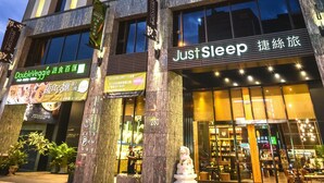 Een hotel met meerdere verdiepingen, verlichte ramen en een bordje met de tekst 'Just Sleep'.