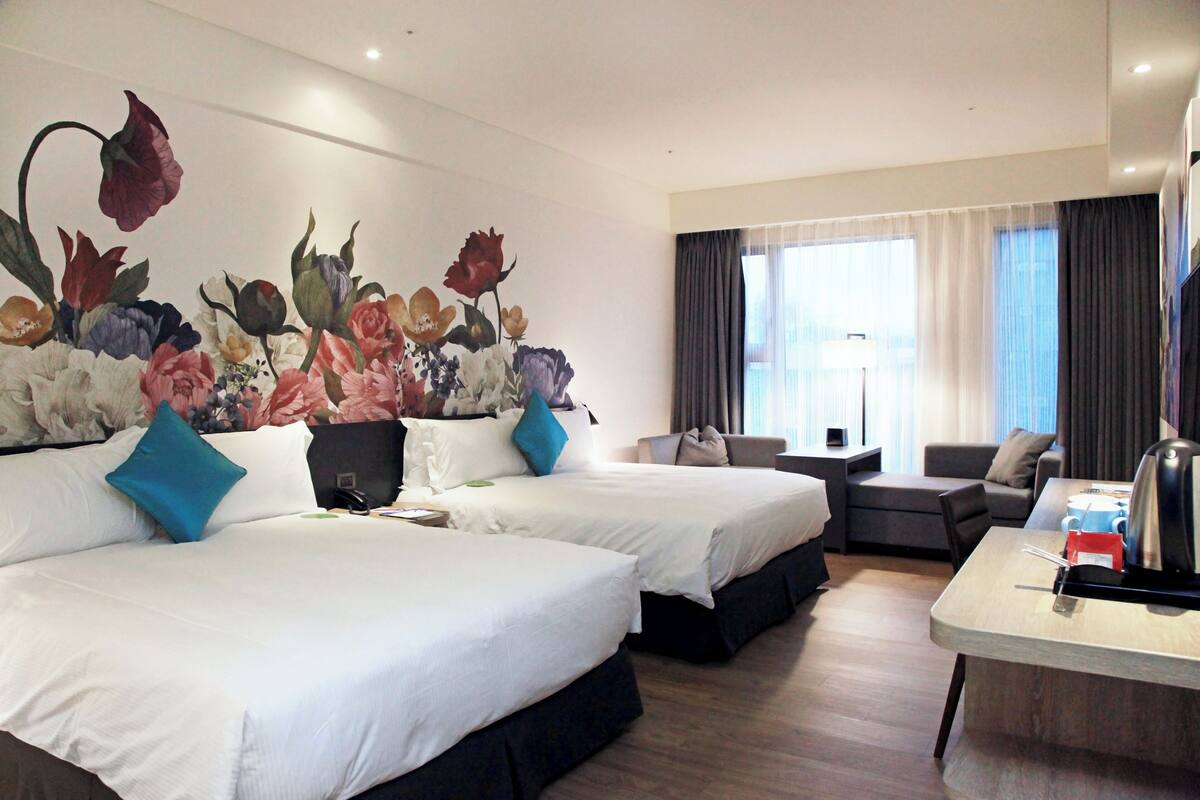 Una habitación de hotel con dos camas, un sofá, una mesita de centro y un gran mural floral en la pared.