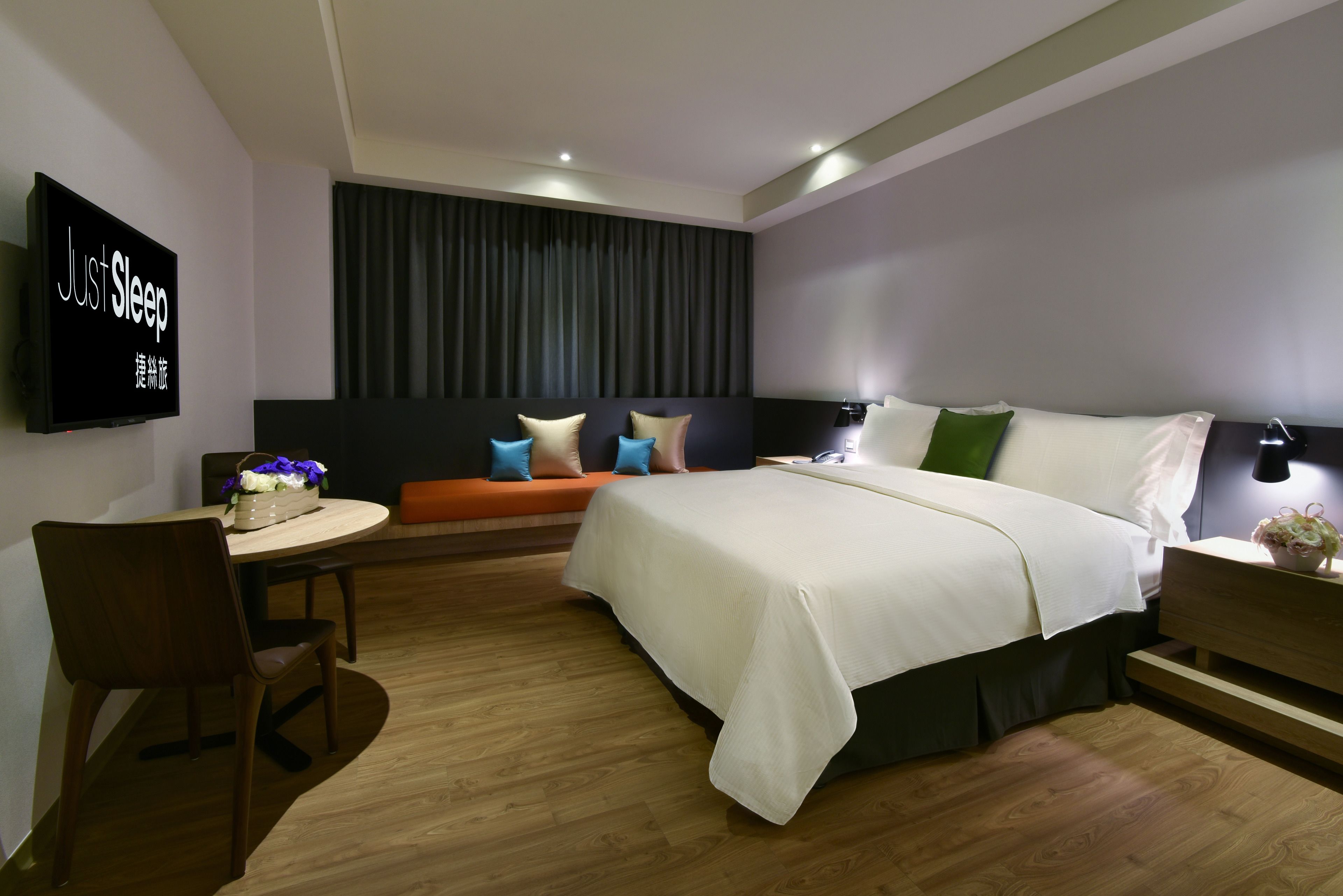 A modern hotel room with a bed, a desk, a chair, a TV, and a sofa.