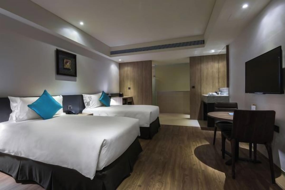A hotel room with two beds, a desk, a chair, and a TV.