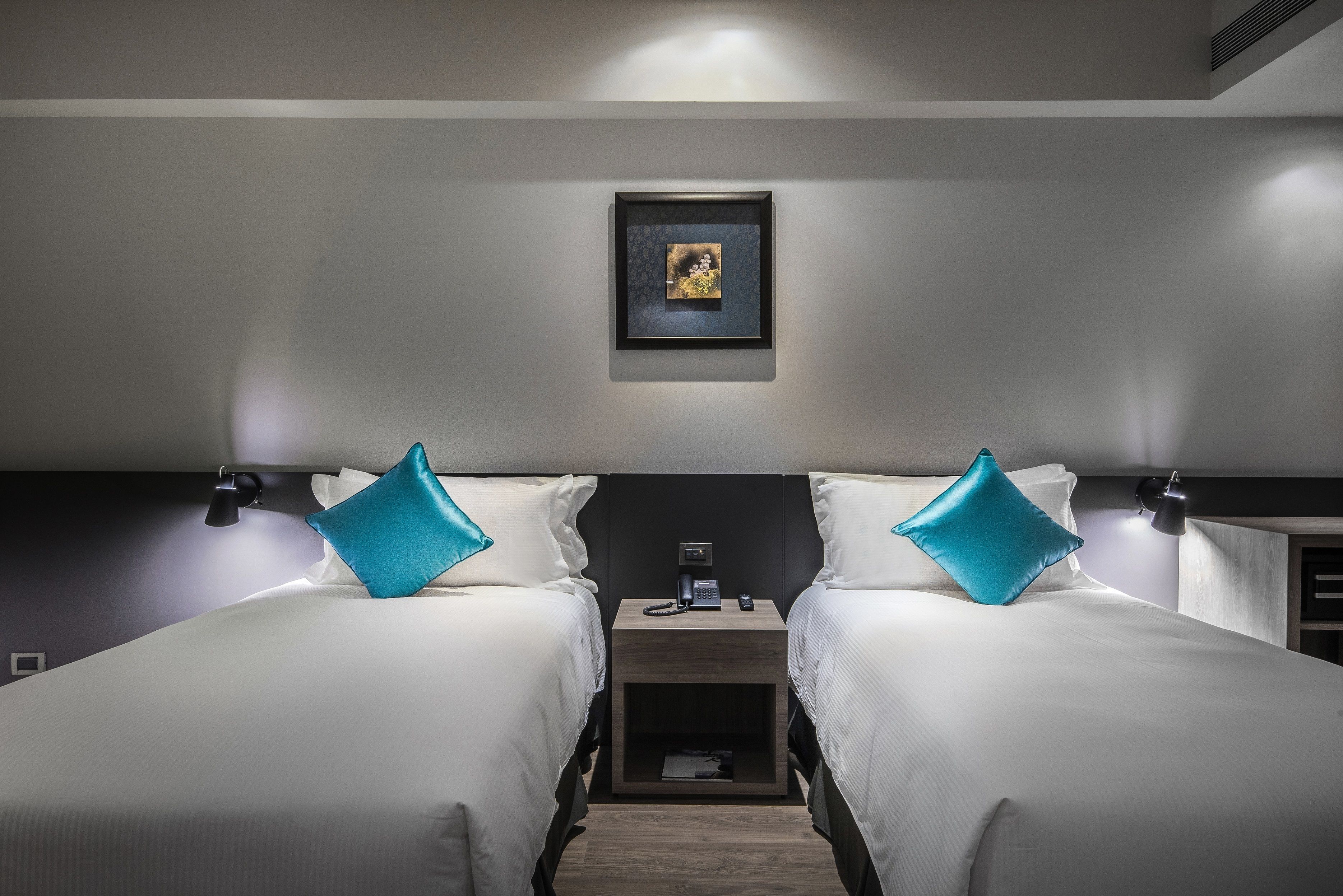 A hotel room with two beds, a nightstand, a phone, and a framed picture on the wall.