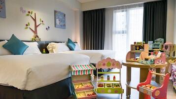 Habitación de hotel con dos camas, zona de juegos infantiles y un ventanal grande con cortinas.