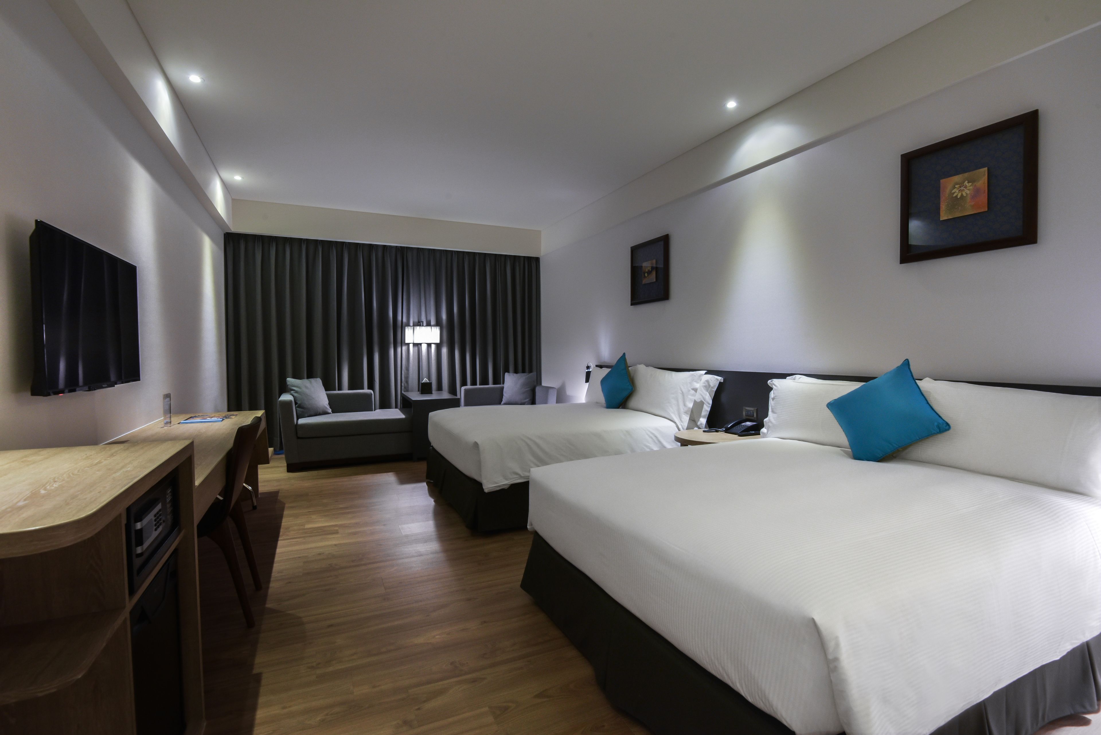 A hotel room with two beds, a desk, a chair, a sofa, and a large window with curtains.