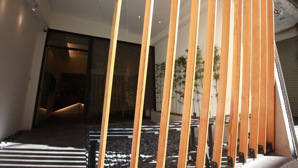 Un interior moderno con una estructura de listones de madera, un camino de piedra y una vista de una habitación con puerta de vidrio.