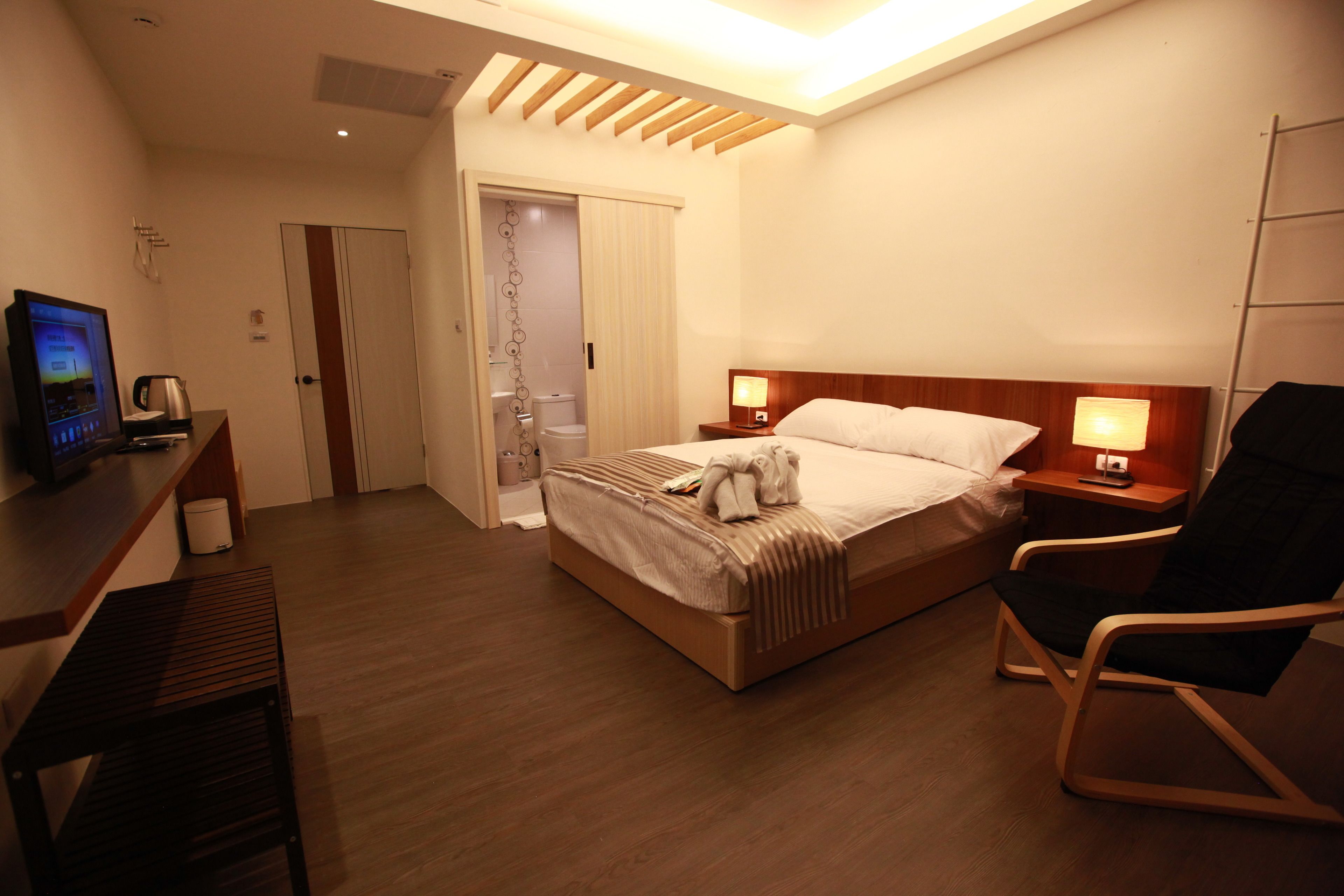 A hotel room with a bed, bedside tables, a desk, a chair, a TV, and a shower area.