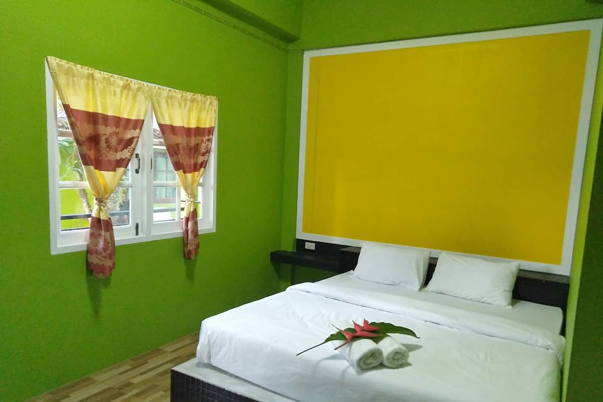 Ein Hotelzimmer mit einem Bett, einem Fenster mit Vorhängen und einer leuchtend gelben Wand.