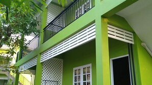 Ein mehrstöckiges Gebäude mit grünen Außenwänden, einem Balkon mit schwarzen Geländern und einer Treppe, die zu den oberen Stockwerken führt.