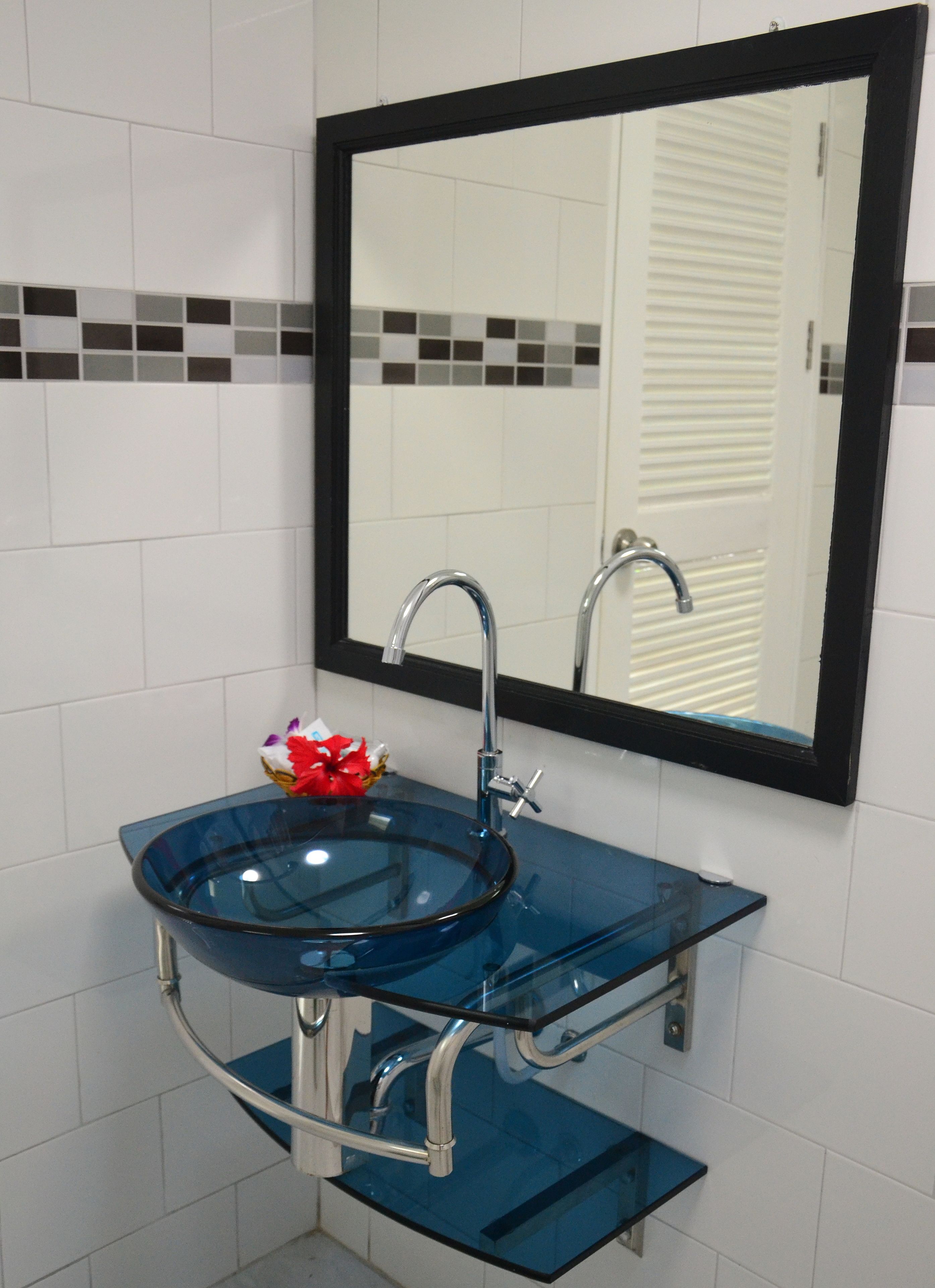 A bathroom with a glass sink, chrome faucet, and a mirror with a black frame.