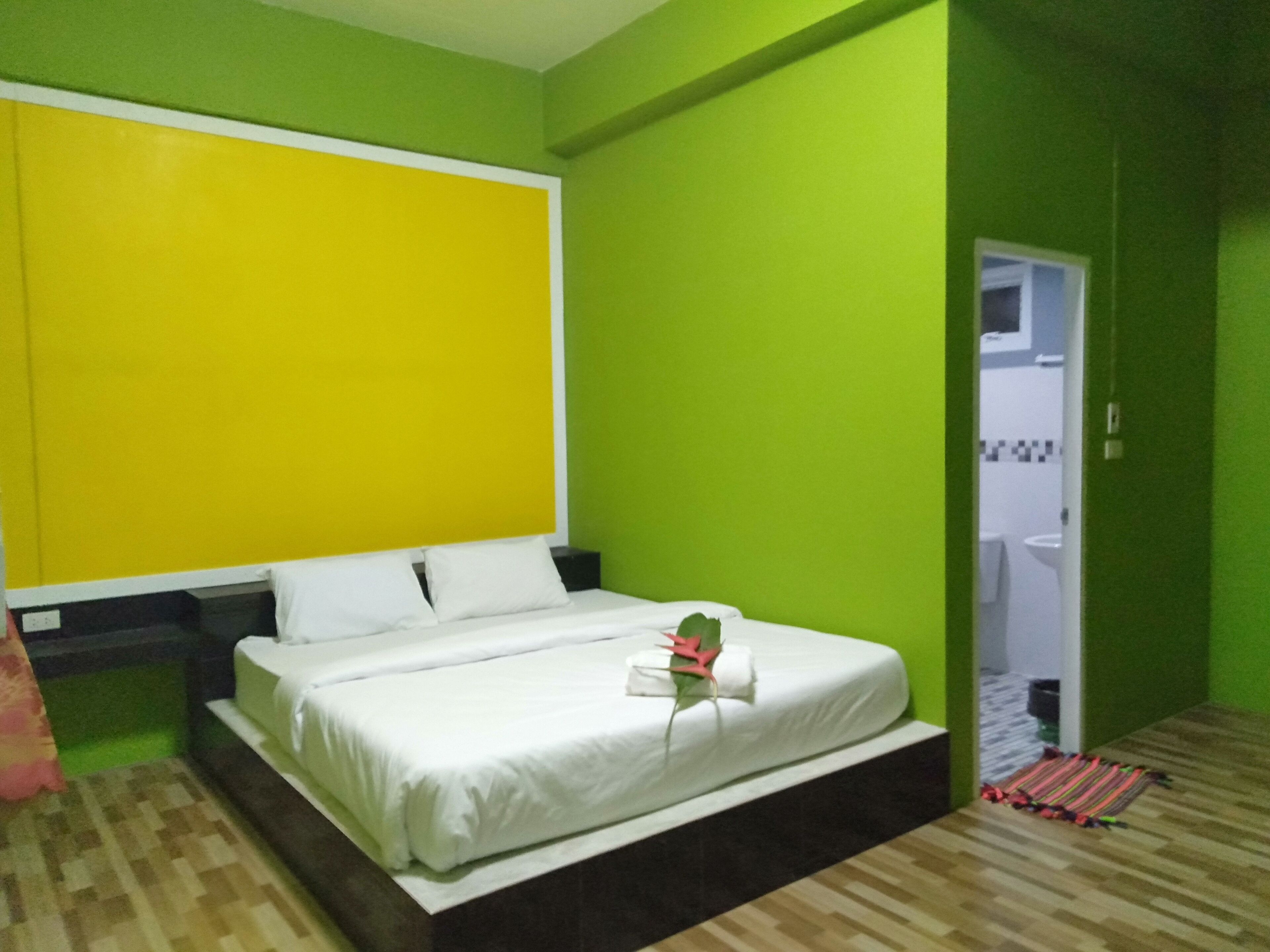 A hotel room with a bed, green walls, and a yellow accent wall.