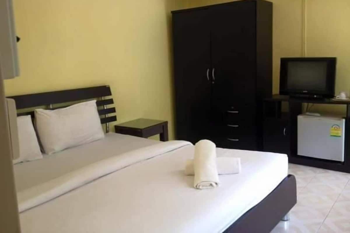 Ein Hotelzimmer mit Bett, Fernseher, Kleiderschrank und kleinem Kühlschrank.