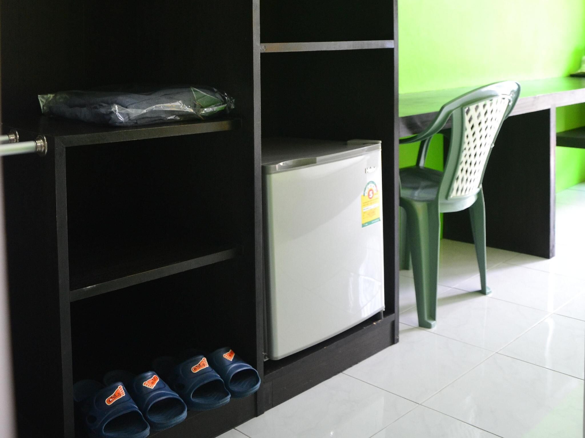 Eine kleine Küchenzeile mit einem Kühlschrank, einem Schuhregal und einem grünen Stuhl.