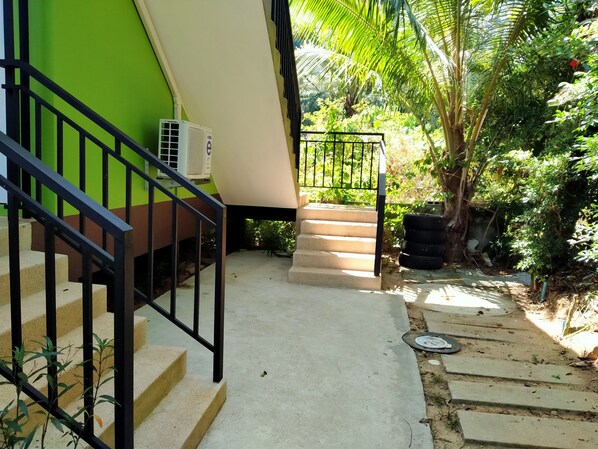 Un escalier mène à un bâtiment aux couleurs vert et blanc, sur lequel on peut voir un appareil de climatisation fixé au mur.