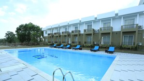 Ein Swimmingpool mit blauen Liegestühlen und ein Gebäude mit Balkonen im Hintergrund.