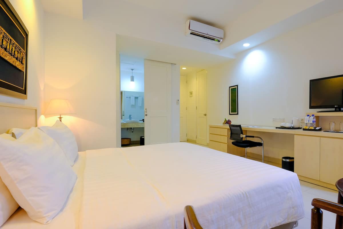 A hotel room with a bed, desk, chair, TV, and a small table with a vase of flowers.