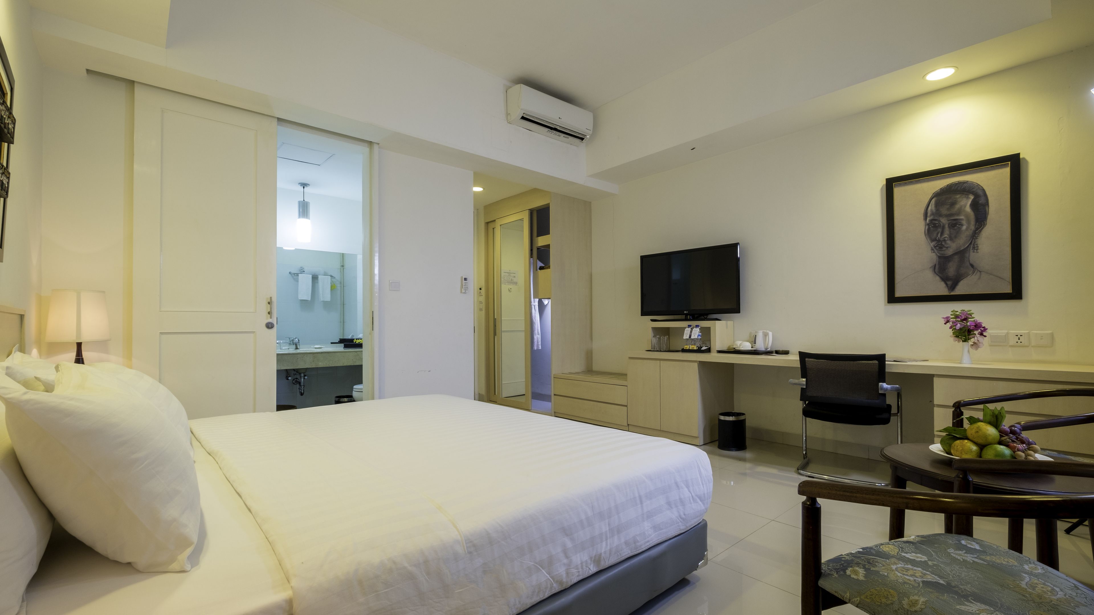 A hotel room with a bed, a desk, a chair, a TV, and a painting on the wall.