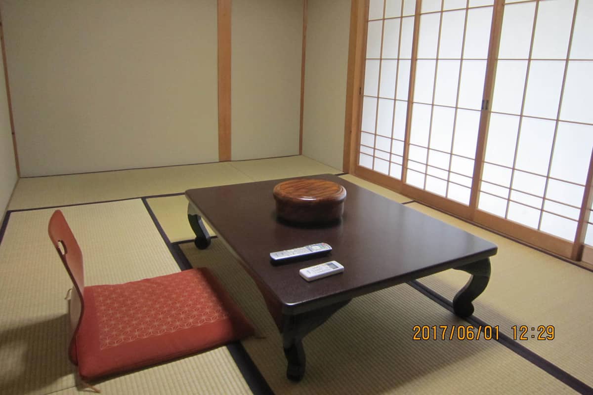Una habitación japonesa tradicional con suelo de tatami, una mesa baja, un cojín rojo y puertas correderas.