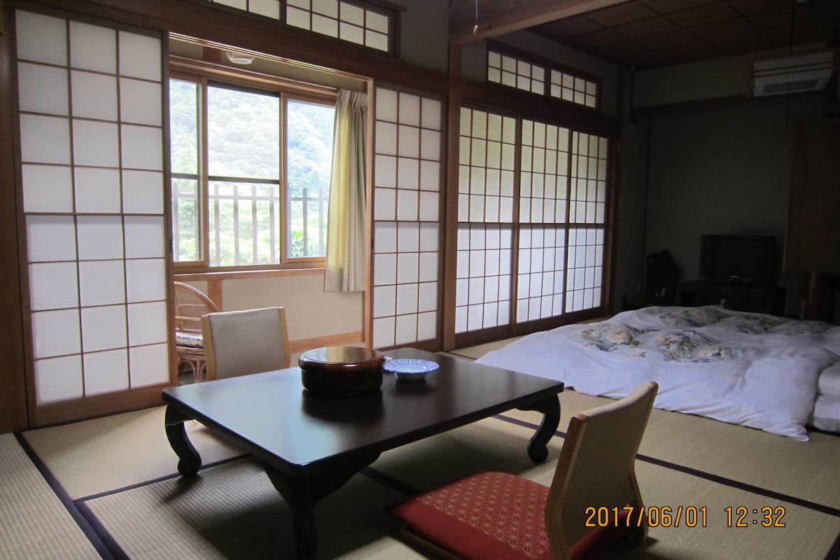 Una habitación japonesa tradicional con suelo de tatami, una mesa baja, una silla, una cama y puertas correderas.