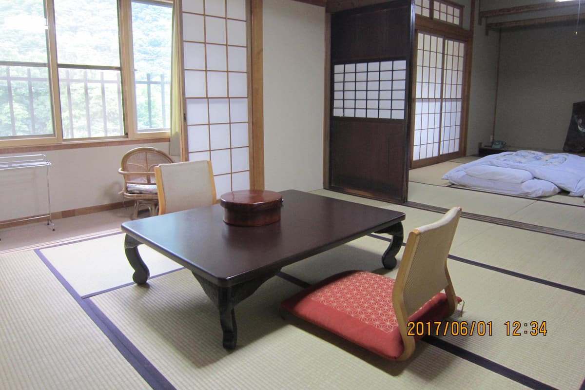 Una habitación tradicional japonesa con suelo de tatami, una mesa baja, una silla y puertas correderas.