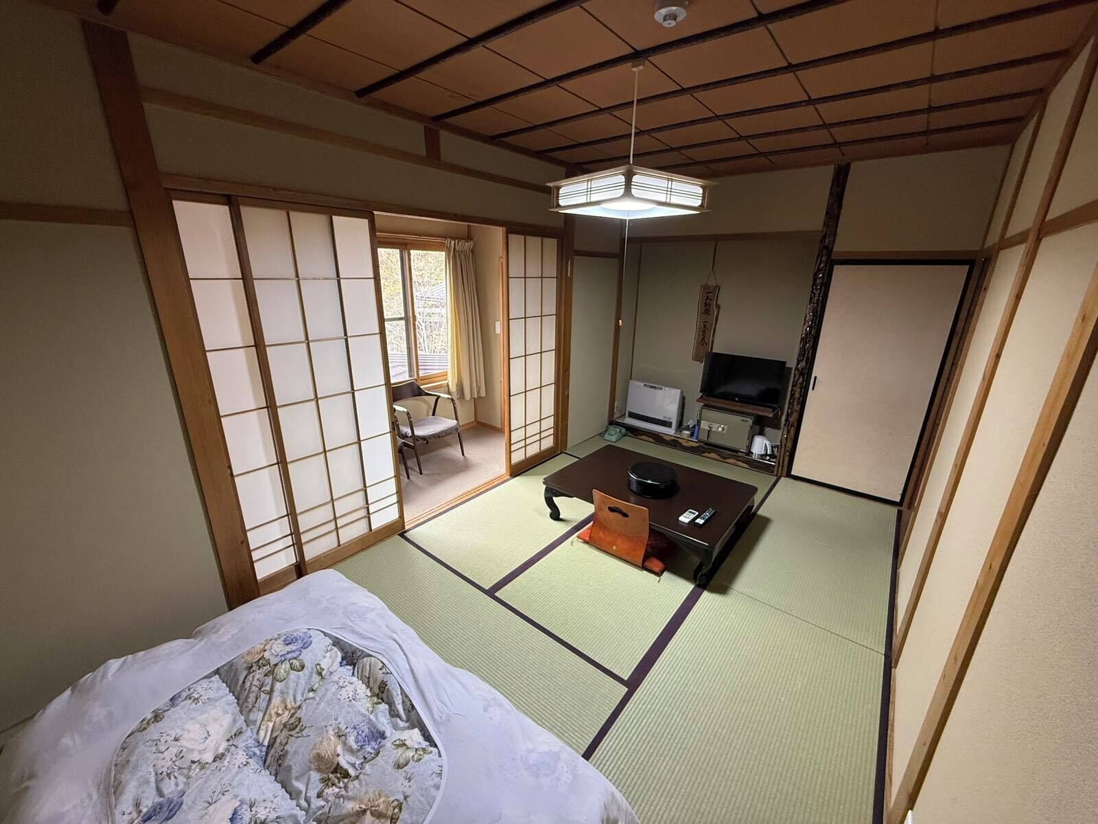 A traditional Japanese room with tatami flooring, a futon bed, a television, and a sliding door.