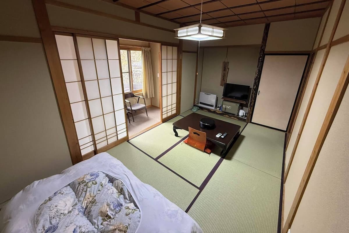 Una habitación japonesa tradicional con suelo de tatami, futón, televisor y puerta corrediza.