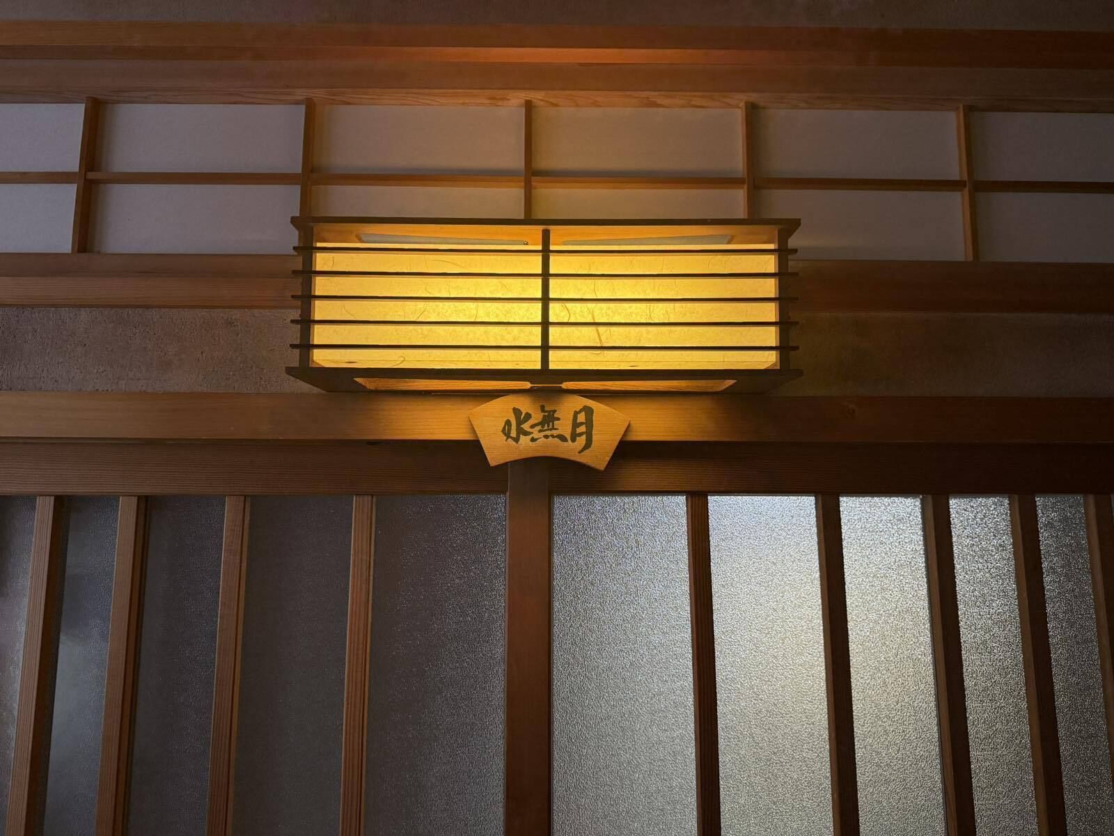 Een traditionele Japanse kamer met een schuifdeur en een houten bord met Japanse tekens.