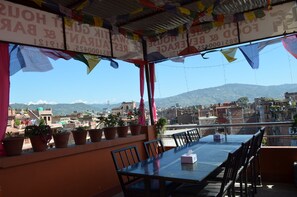 A dining area with a table and chairs, potted plants, and a view of a cityscape with mountains in the background. - Swastik Guest House (Bhaktapur)
