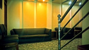 A living room with a sofa, chairs, and a patterned carpet. There is a staircase with a metal railing. - Swastik Guest House (Bhaktapur)